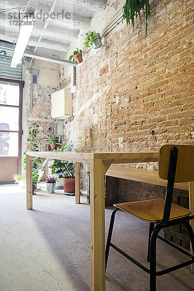 Stuhl und leerer Tisch stehen drinnen vor einer Backsteinmauer