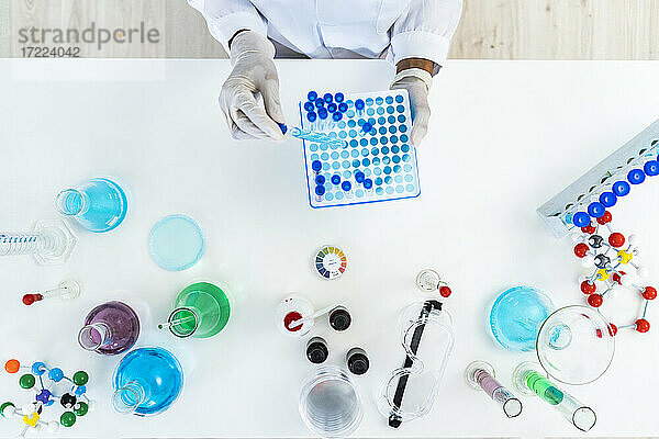Eine Forscherin entnimmt ein Reagenzglas aus einer Mikroplatte auf einem Tisch im Labor