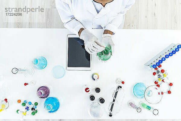 Eine Forscherin testet eine Flüssigkeit in einem Kolben auf einem Tisch im Labor