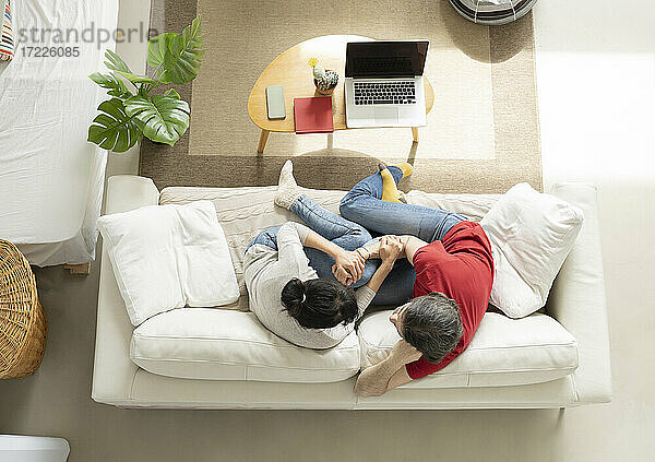 Zärtliches Paar,  das sich umarmt,  während es auf dem Sofa im Wohnzimmer sitzt