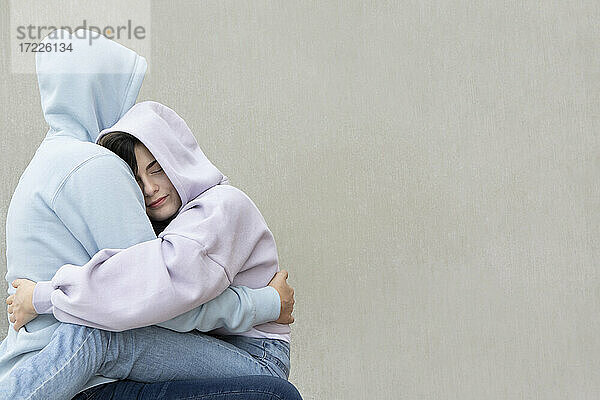 Mädchen umarmt,  während sie auf dem Schoß ihres Freundes an der Wand sitzt