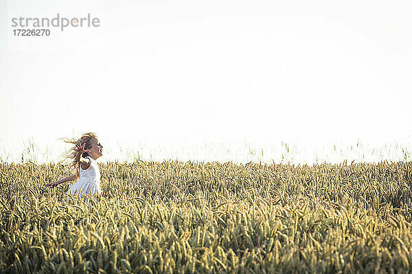 Mädchen mit zerzaustem Haar läuft bei Sonnenuntergang durch ein landwirtschaftliches Feld