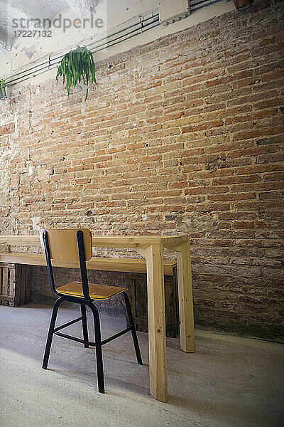 Stuhl und leerer Tisch stehen drinnen vor einer Backsteinmauer