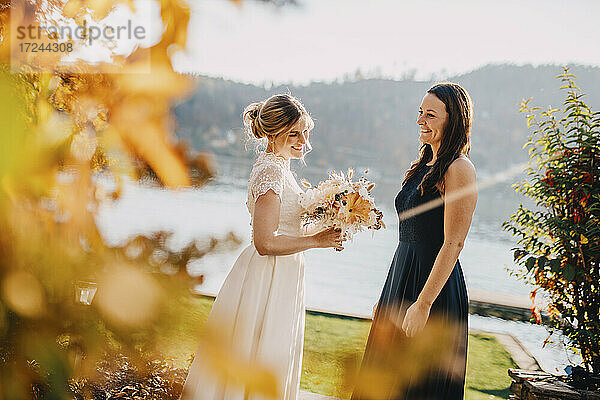Glückliche Braut hält Blumenstrauß,  während sie mit einem Freund steht