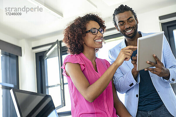 Lächelnder Mann und lächelnde Frau benutzen ein digitales Tablet im Büro