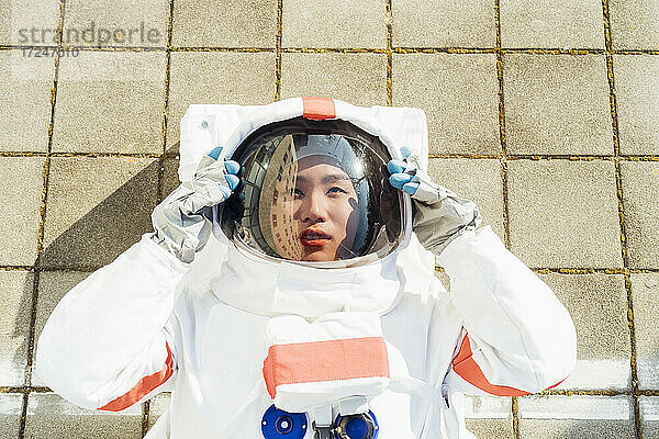 Weibliche Astronautin mit Helm auf dem Gehweg liegend an einem sonnigen Tag