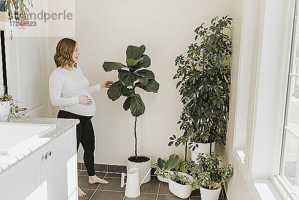 Lächelnde Frau betrachtet eine Topfpflanze im Wohnzimmer