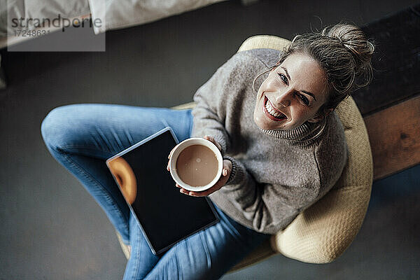 Glückliche Besitzerin hält eine Cappuccino-Schale,  während sie in einem Café sitzt