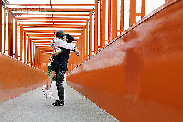 Teenager-Paar küsst sich auf orangefarbener Brücke