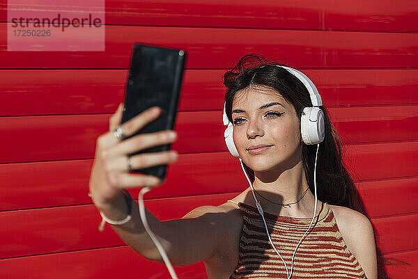 Lächelndes Teenager-Mädchen,  das ein Selfie über ein Smartphone macht,  während es Musik hört