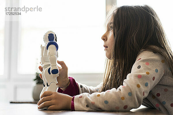 Nachdenkliches Mädchen,  das wegschaut,  während es ein Roboterspielzeug zu Hause hält