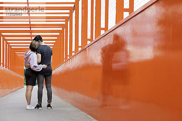 Teenagerpaar umarmt sich auf einer orangefarbenen Brücke