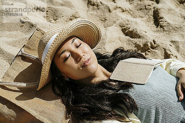 Frau mit geschlossenen Augen im Sand liegend an einem sonnigen Tag
