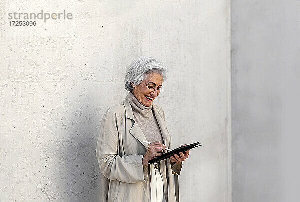 Glückliche Frau mit digitalem Tablet vor einer Wand