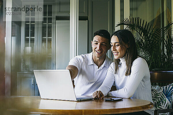 Lächelnder Mann und lächelnde Frau benutzen einen Laptop,  während sie zu Hause sitzen