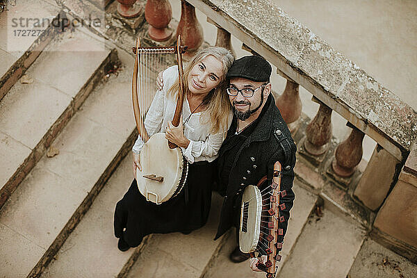 Lächelnder Mann und lächelnde Frau halten ein Lyra-Musikinstrument auf einer Treppe