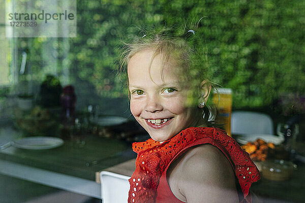 Lächelndes Mädchen schaut durch ein Fenster an einem sonnigen Tag