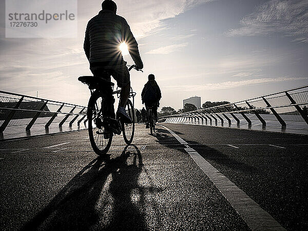 Dänemark,  Kopenhagen,  Silhouetten von zwei Menschen auf Fahrrädern über die Langebro-Brücke bei Sonnenuntergang