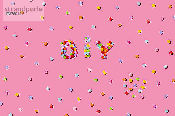DIY Text arrangiert mit bunten Pom Poms auf rosa Hintergrund