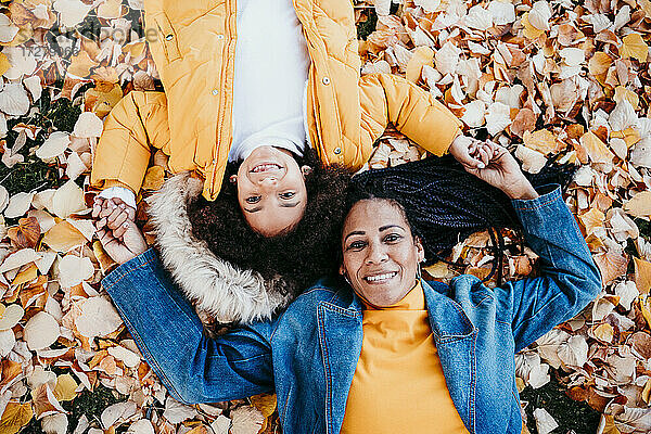 Lächelnde Mutter und Tochter liegen im Park auf gefallenen Blättern