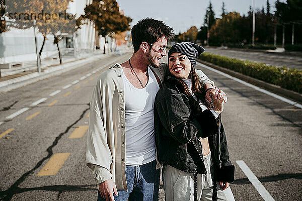 Lächelnde Frau hält Hände mit männlichem Partner,  während sie auf der Straße in der Stadt steht
