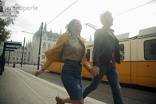Glückliche Frau hält Hände mit männlichem Partner beim Laufen in der Stadt