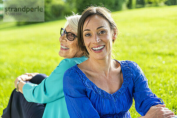 Glückliche Frau im mittleren Erwachsenenalter mit älterer Frau im öffentlichen Park sitzend