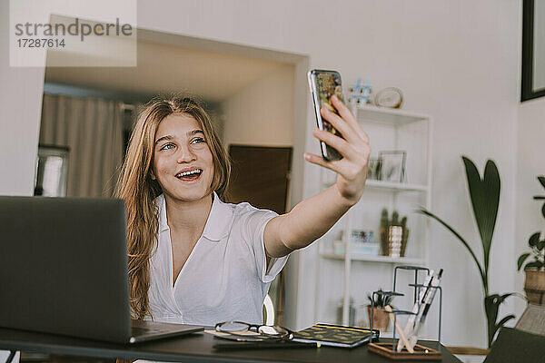 Lächelndes Mädchen,  das über ein Smartphone zu Hause einen Videoanruf tätigt