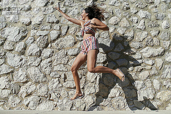 Frau gestikuliert beim Sprung durch eine Steinmauer