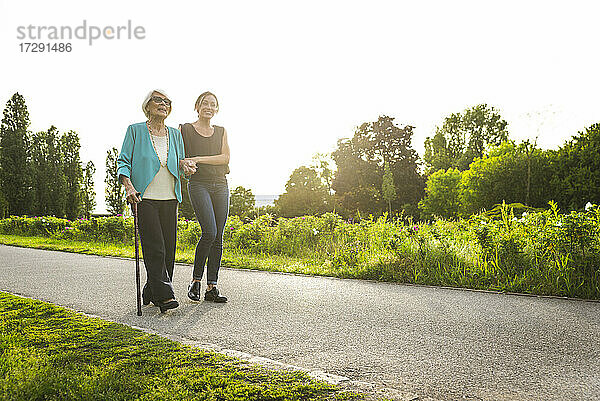 Mittlere erwachsene Frau,  die eine ältere Frau beim Spazierengehen im Park stützt