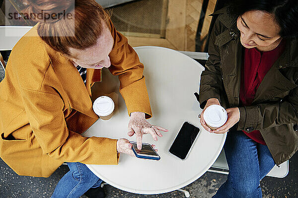 Frau zeigt einer Freundin ihr Smartphone,  während sie im Cafe sitzt