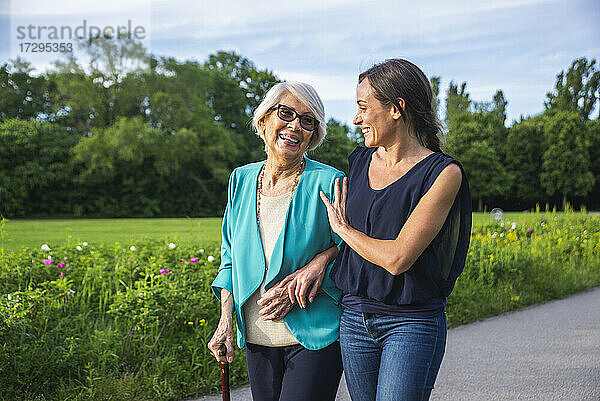 Pflegende Frau im mittleren Erwachsenenalter mit älterer Frau beim Spaziergang im Park