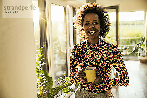 Glückliche Frau hält Kaffeetasse zu Hause