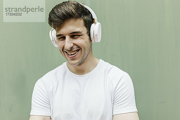 Glücklicher Mann mit Kopfhörern vor einer grünen Wand