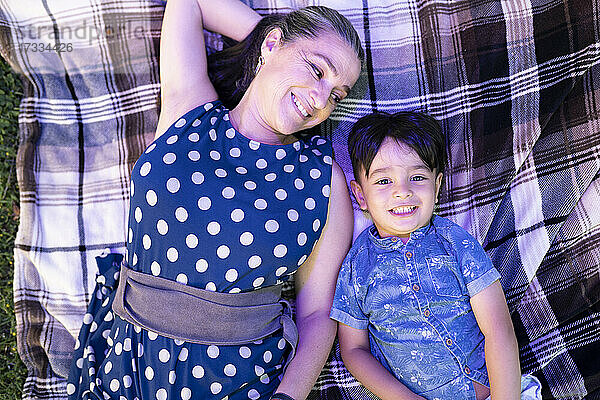 Lächelnde reife Frau sieht ihren Enkel an,  während sie sich auf einer Decke ausruht
