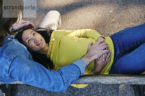 Lächelnde Frau sieht ihren Mann an,  während sie auf dem Schoß im Park liegt