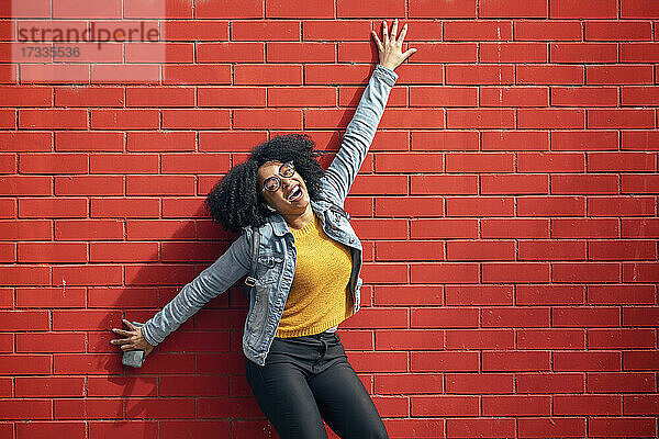 Glückliche junge Frau lehnt an einer roten Backsteinmauer