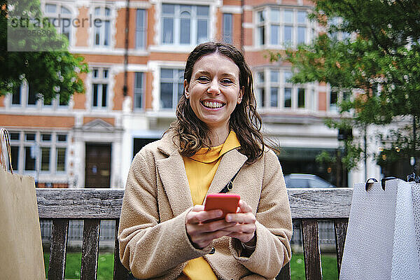 Glückliche junge Frau mit Smartphone auf einer Bank sitzend