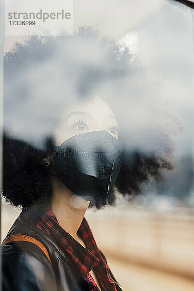 Nachdenkliche Frau mit Gesichtsschutzmaske schaut durch eine Glaswand