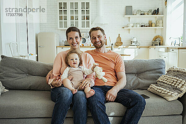 Lächelnder Mann und lächelnde Frau auf dem Sofa mit Tochter auf dem Schoß zu Hause