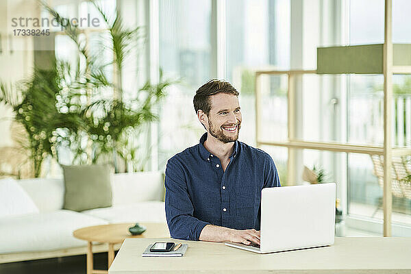Glücklicher männlicher Berufstätiger mit Laptop im Heimbüro sitzend