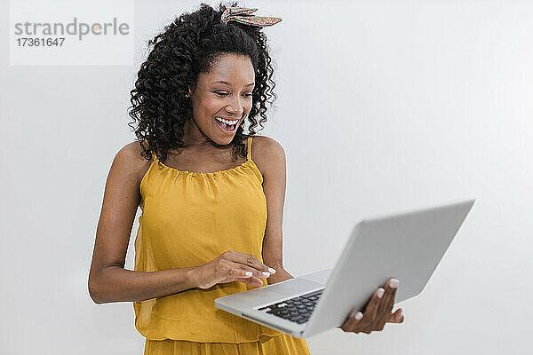 Glückliche junge Frau mit Laptop vor weißem Hintergrund