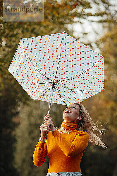 Fröhliche Frau schaut auf umgedrehten Regenschirm