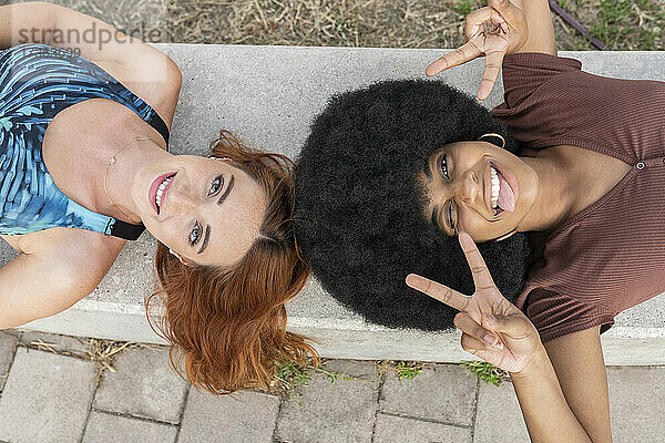 Afro-Frau gestikuliert Friedenszeichen,  während sie mit einer Freundin auf einer Bank liegt