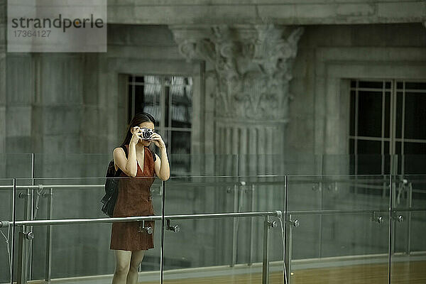 Weibliche Touristin fotografiert durch die Kamera,  während sie an einem Glasgeländer steht