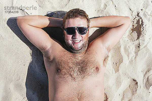 Lächelnder schwuler Mann,  der sich an einem sonnigen Tag im Sand entspannt