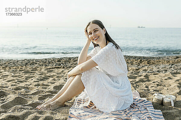 Glückliche schöne Frau sitzt auf Strandtuch