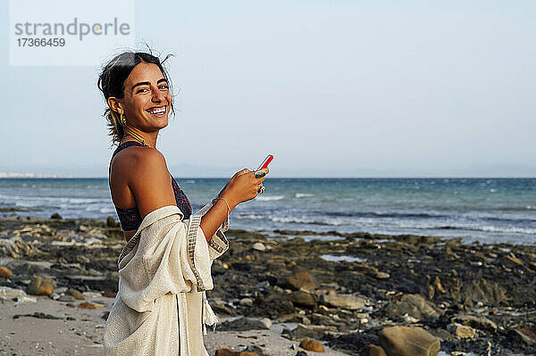 Glückliche junge Frau hält Handy am Strand