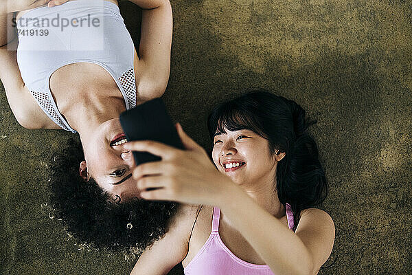 Lächelnde Freunde machen Selfies mit dem Handy,  während sie auf dem Boden liegen