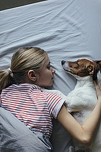 Blondes Mädchen liegt auf dem Bett und kuschelt mit ihrem Hund
